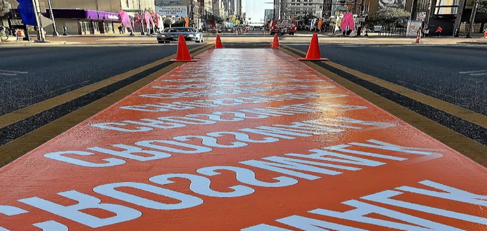 Bright orange crosswalk featuring the word 'CROSSWALK' printed repeatedly along its length.