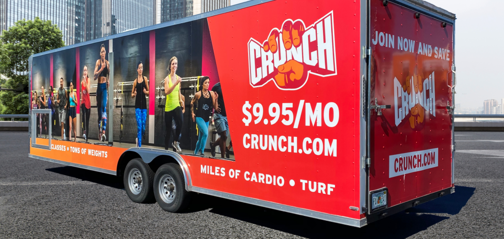 Red trailer with Crunch Fitness branding and images of people exercising on the sides.