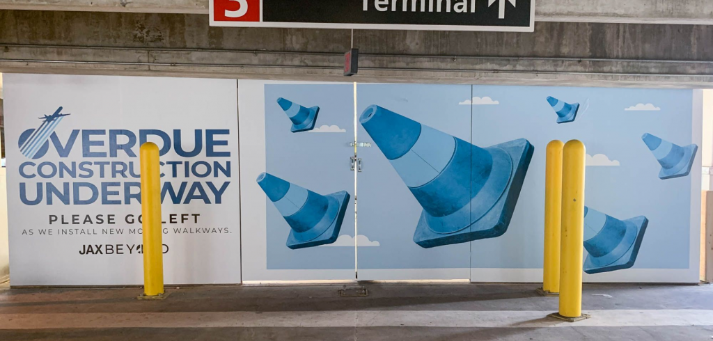 Mural depicting traffic cones with the text 'Overdue Construction Underway' on a wall in a parking area.
