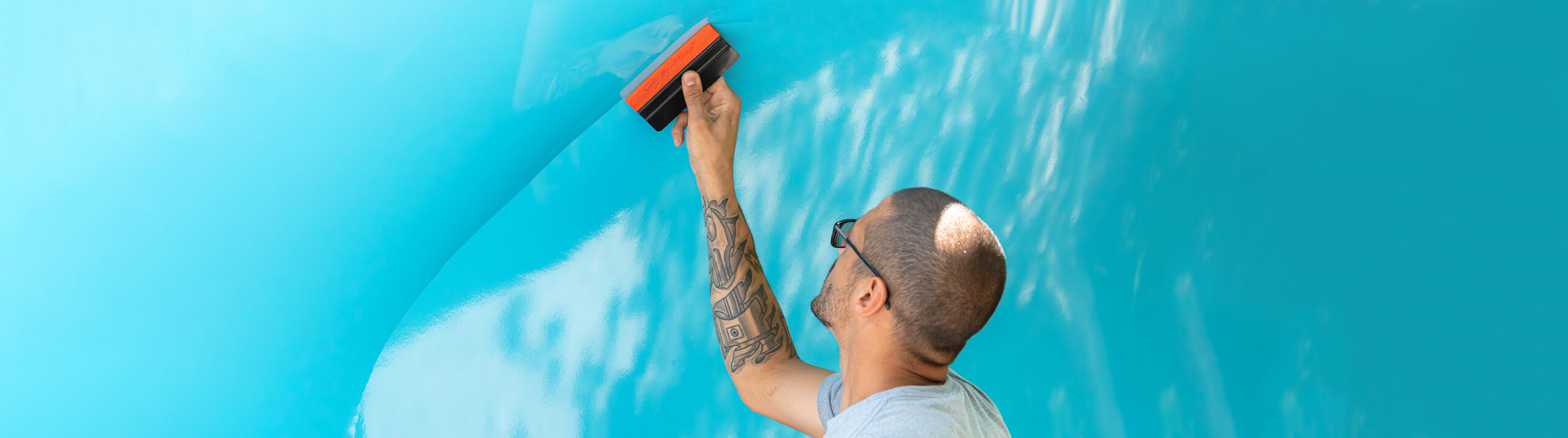 Individual using a tool to apply a blue wrap to a smooth surface.